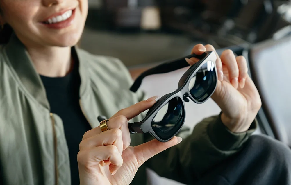 Smaidoša sieviete tur rokās melnas paplašinātās realitātes brilles