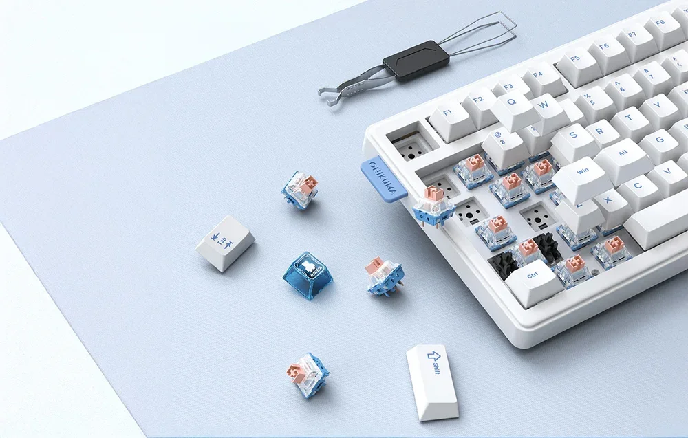 White Onikuma keyboard with removed keys and switch replacement tool on white-blue background
