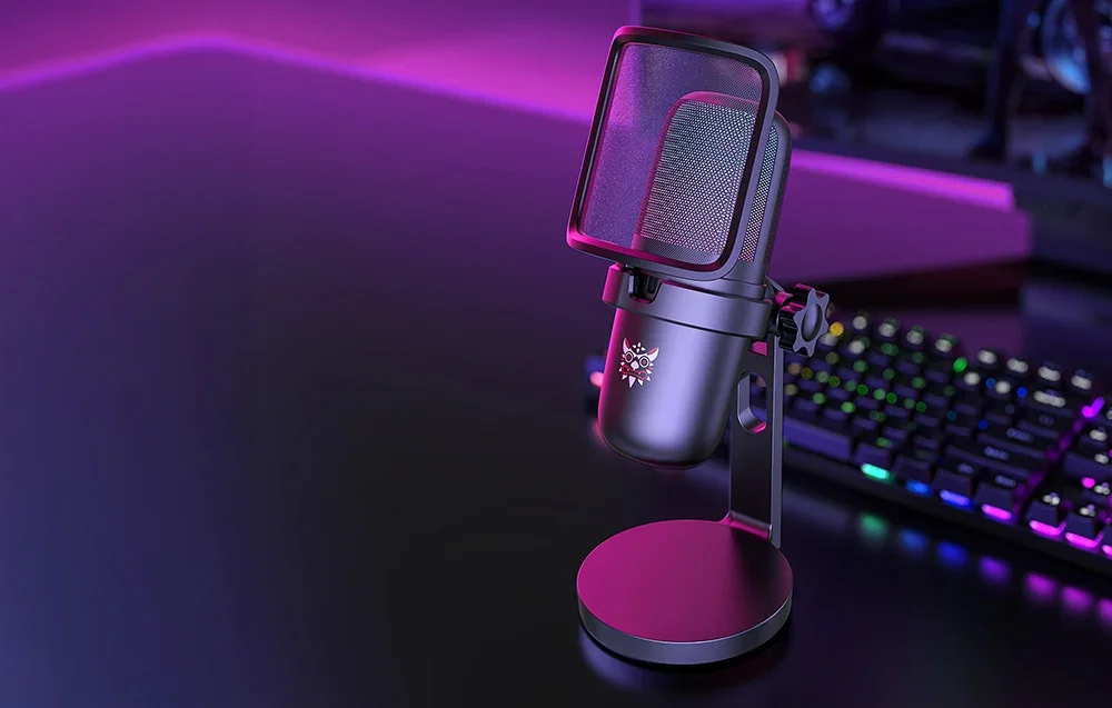 Black Onikuma gaming microphone on the desk, keyboard and monitor in the distance