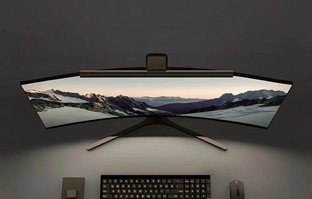 Curved ultra-widescreen monitor with top lamp displaying mountain landscape at dusk