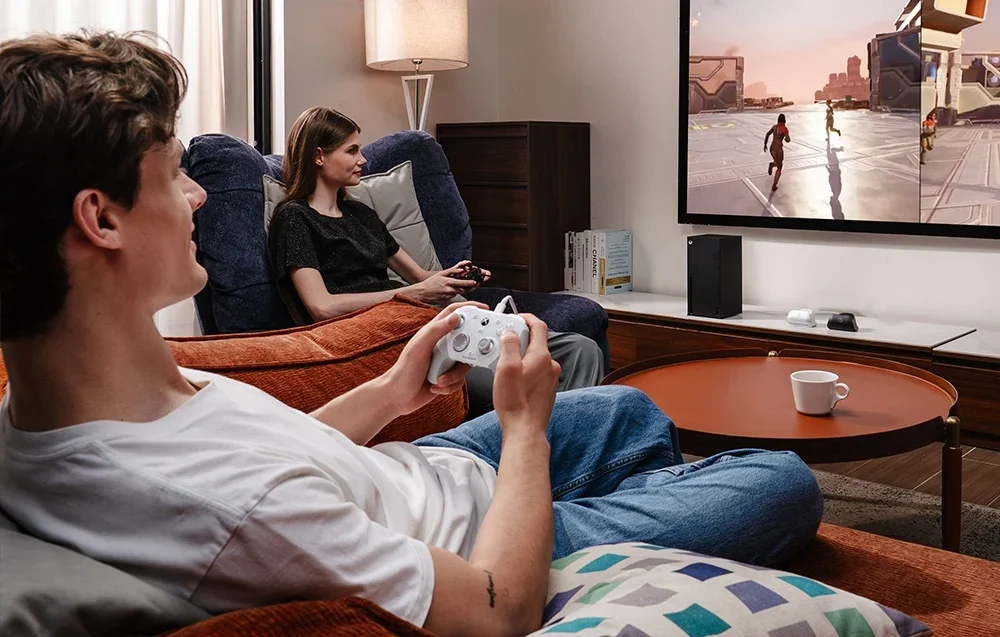 Divi cilvēki spēlē pie televizora ar GameSir kontrolieriem, viens balts un viens melns.