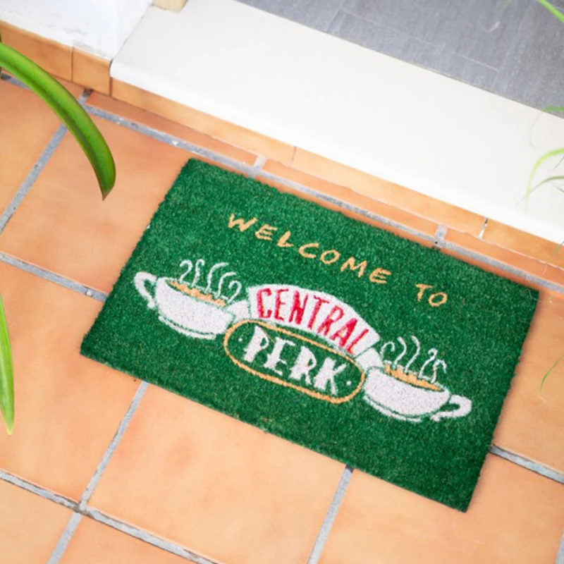 Zaļš Central Perk durvju paklājs pie durvīm uz flīžu grīdas