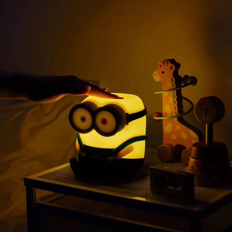 Roka pieskaras iedegtās Minions Boba lampiņas augšdaļai pie gultas